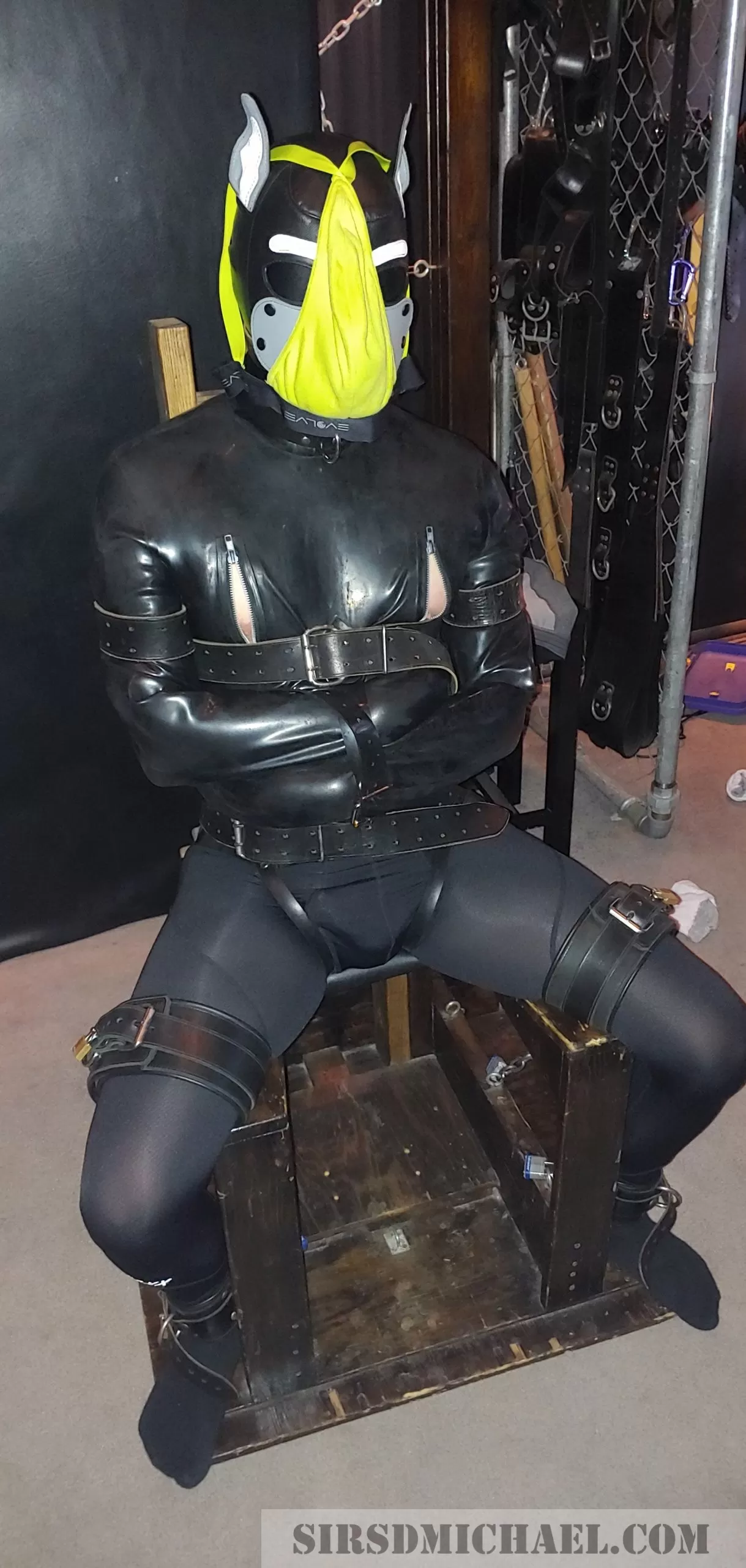 Pup bound in a rubber straitjacket, gagged, and strapped to a bondage chair